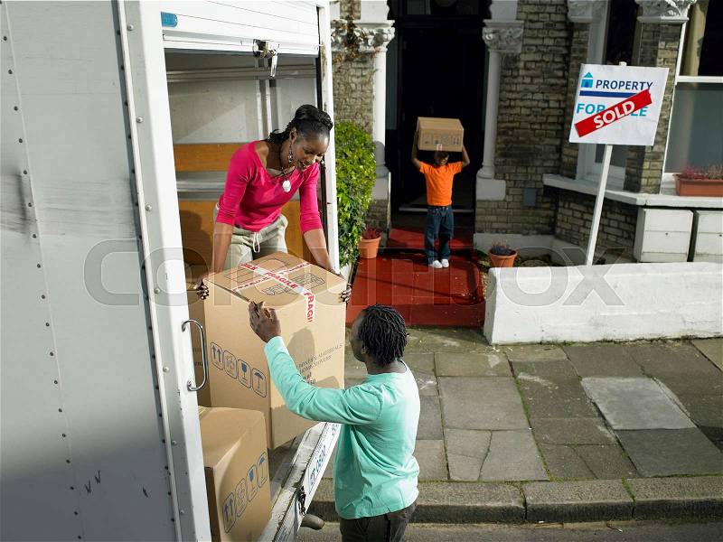 Family unpacking boxes from moving van, stock photo