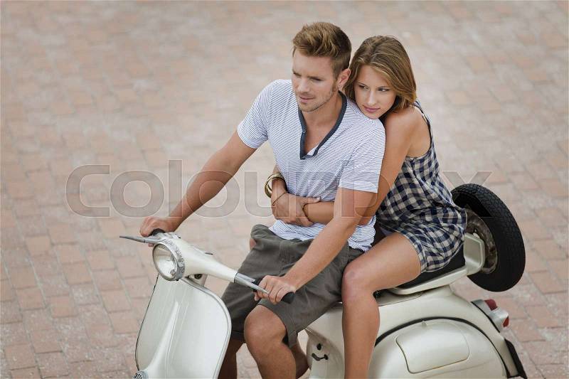 Couple riding scooter together, stock photo