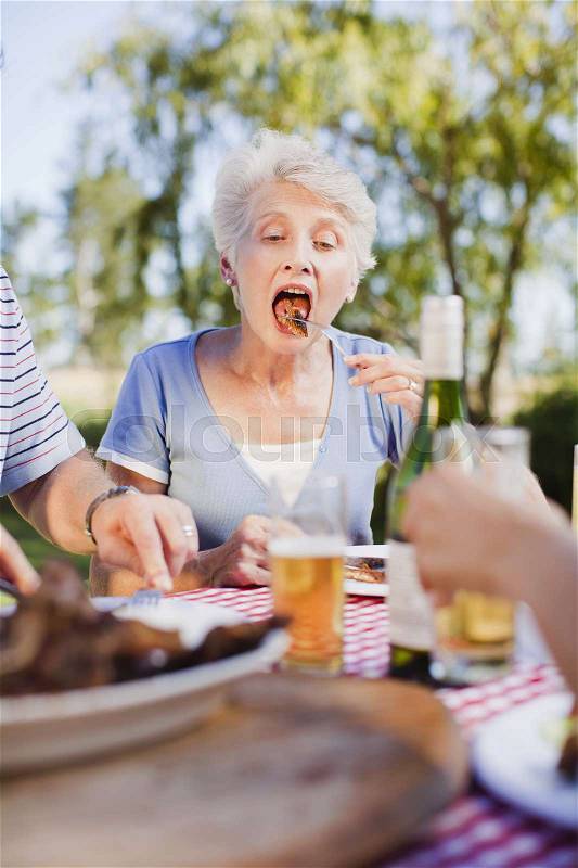 Older woman eating at picnic table, stock photo