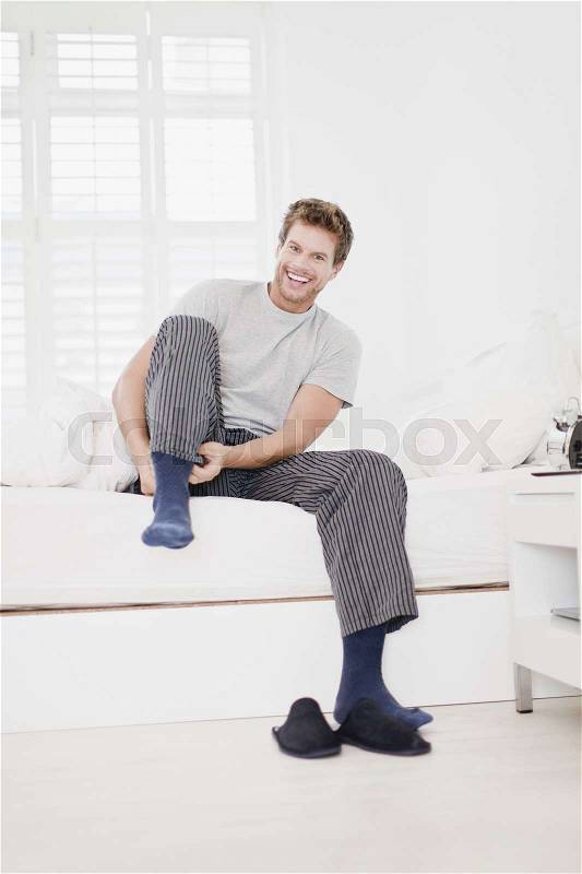 Man putting socks on in bed, stock photo