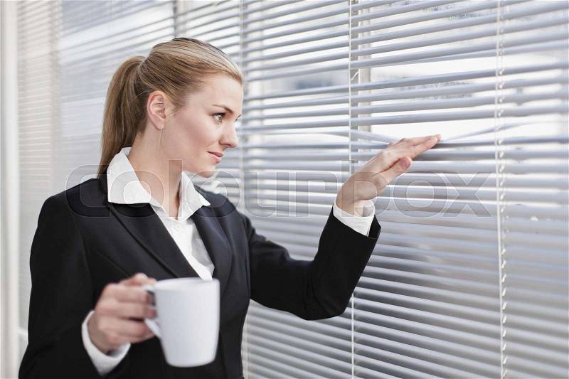 Businesswoman peering out of blinds, stock photo