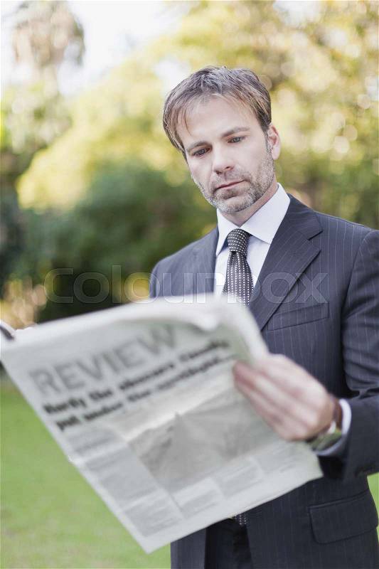 Businessman reading newspaper in park, stock photo