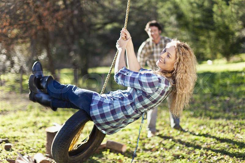 Man pushing girlfriend on tire swing, stock photo