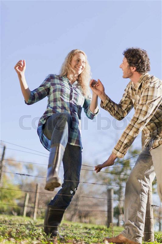 Couple climbing over wire fence outdoors, stock photo