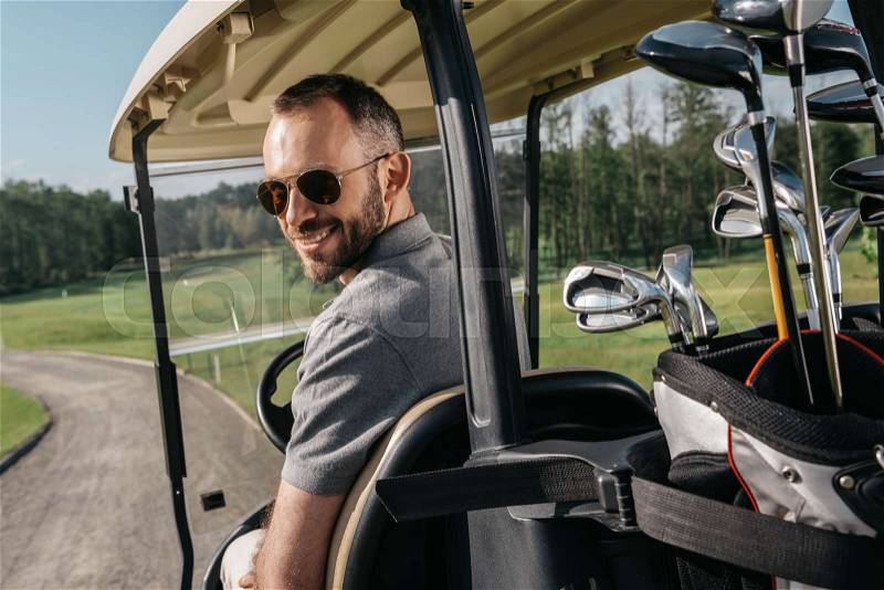 Smiling man in sunglasses riding golf cart and looking at camera, stock photo
