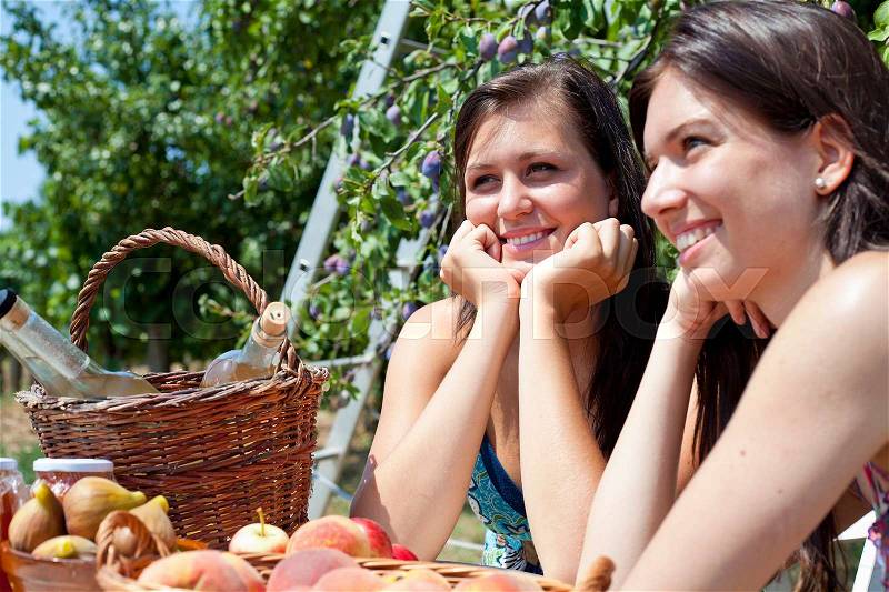 Smiling women picnicking in orchard, stock photo