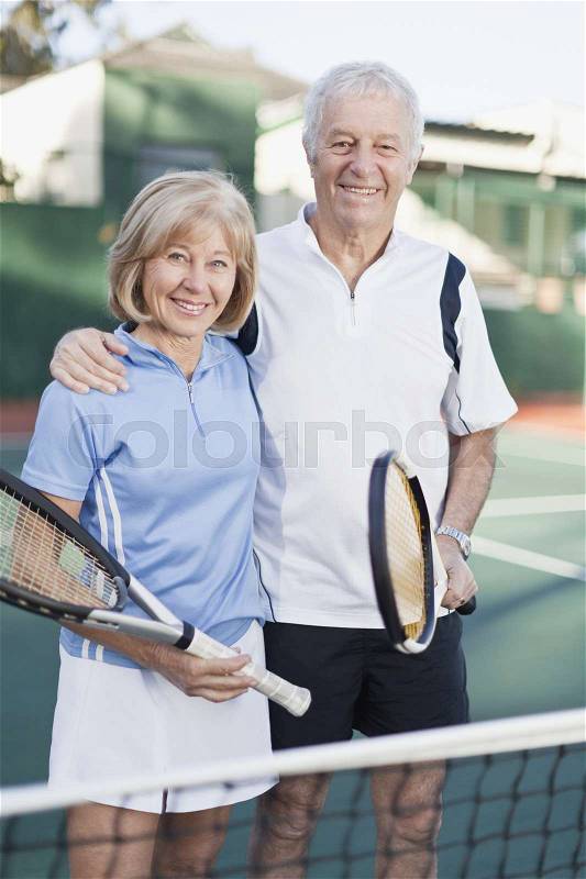 Older couple standing on tennis court, stock photo