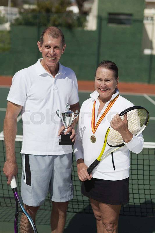 Older couple with trophy on tennis court, stock photo