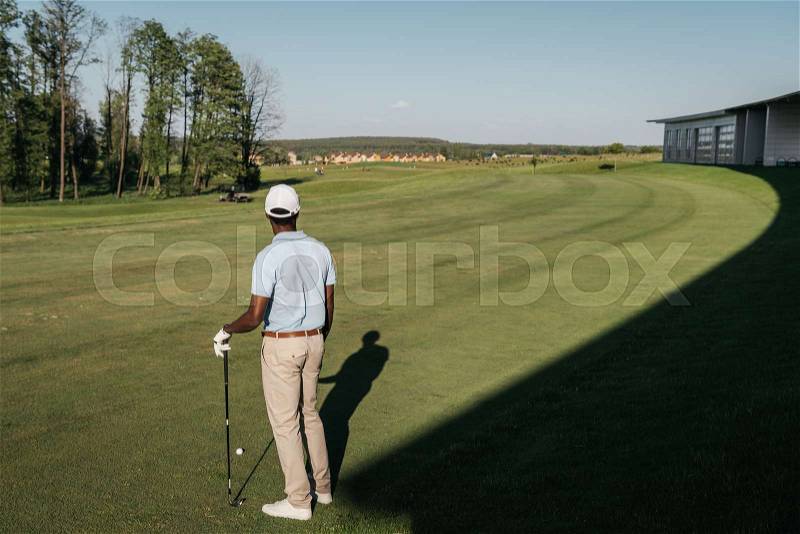 Back view of african american man playing golf with club and ball at green lawn, stock photo