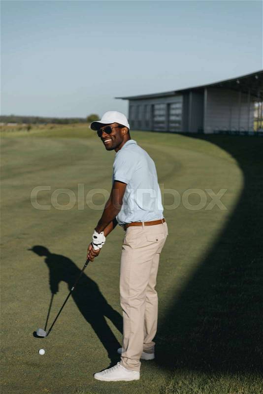 Stylish smiling african american man playing golf on golf course, stock photo
