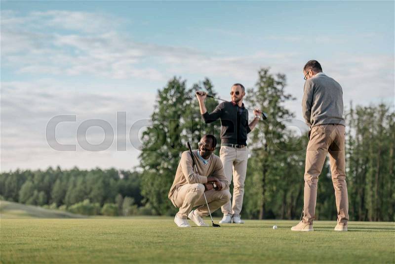 Stylish multicultural friends spending time together while playing golf on golf course , stock photo