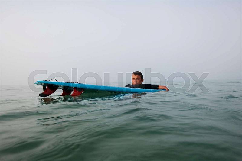 Man floating with surfboard in the water, stock photo