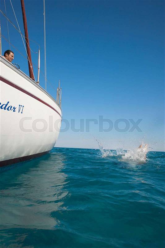 Young woman splashing in sea by yacht, stock photo