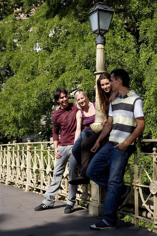 Four friends leaning on bridge rail, stock photo