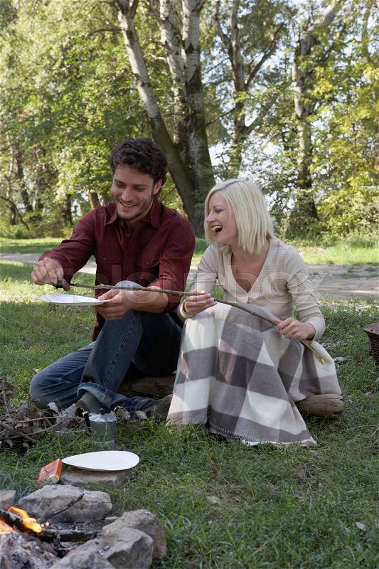 Couple at campsite cooking hotdogs, stock photo
