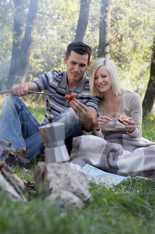 Couple at campsite cooking hot dogs, stock photo