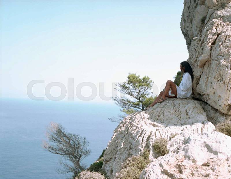Woman sitting on large rocks by the sea, stock photo