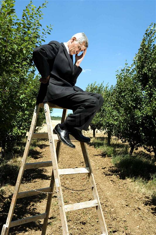 Man sitting on ladder holding his head, stock photo