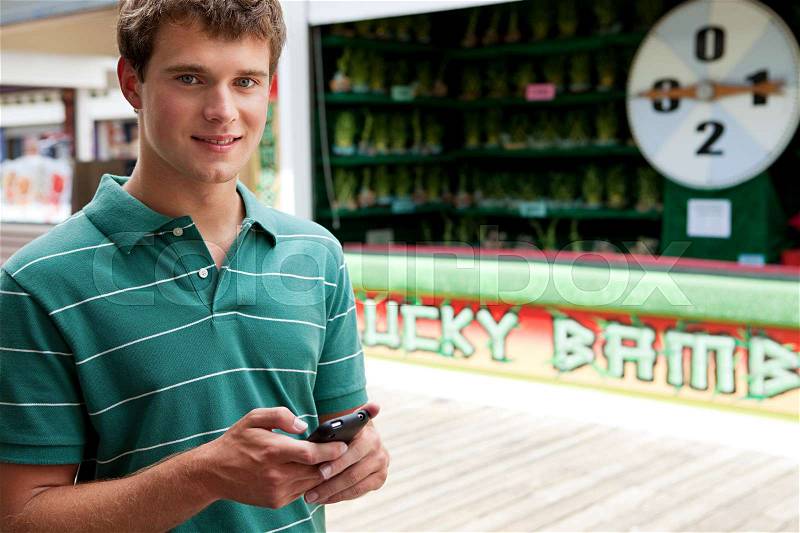 Teenage boy using cellphone at fun fair, stock photo