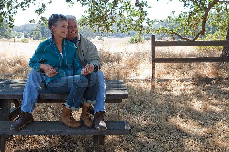 Mature couple sitting on picnic table, stock photo