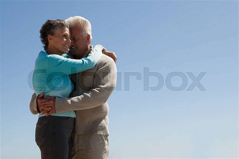 Mature couple hugging against blue sky, stock photo