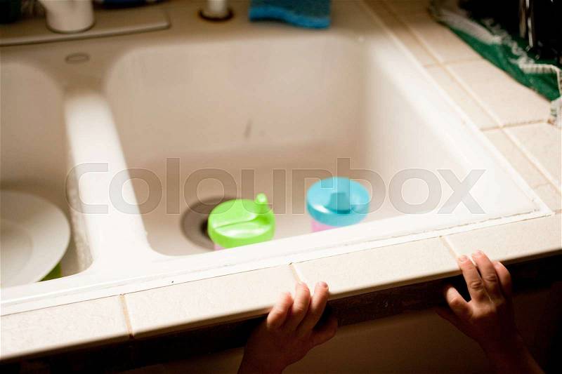 Child reaching towards kitchen sink with beakers, stock photo