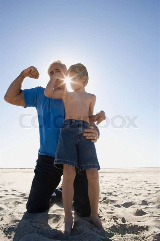 Grandfather and son flexing biceps on beach, stock photo