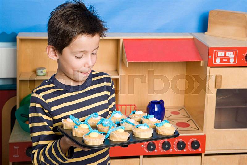Boy holding baking tray of fairy cakes, stock photo