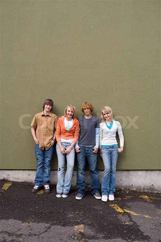 Four teenagers leaning against a wall, stock photo