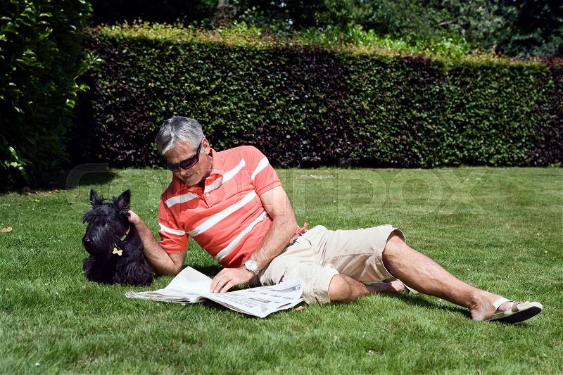 Mature man laying on grass reading paper, stock photo