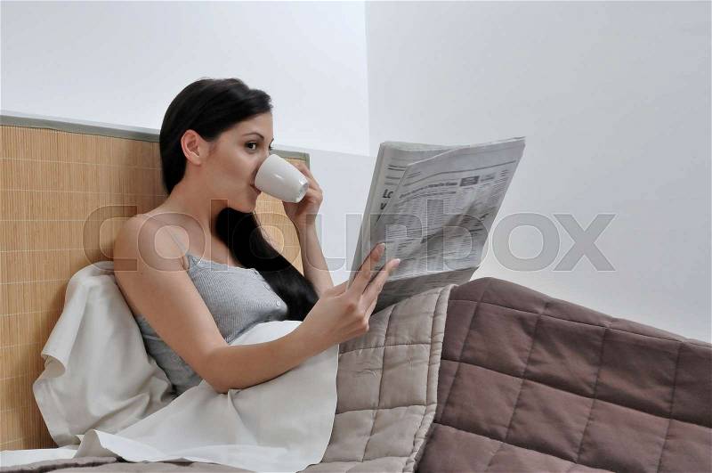 Woman reading paper in her bed, stock photo