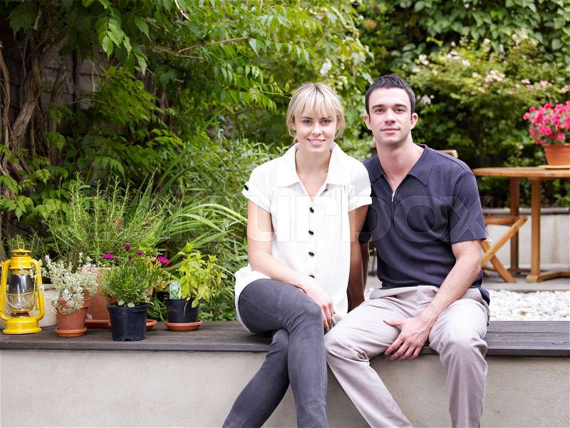 Couple sitting in garden facing camera, stock photo