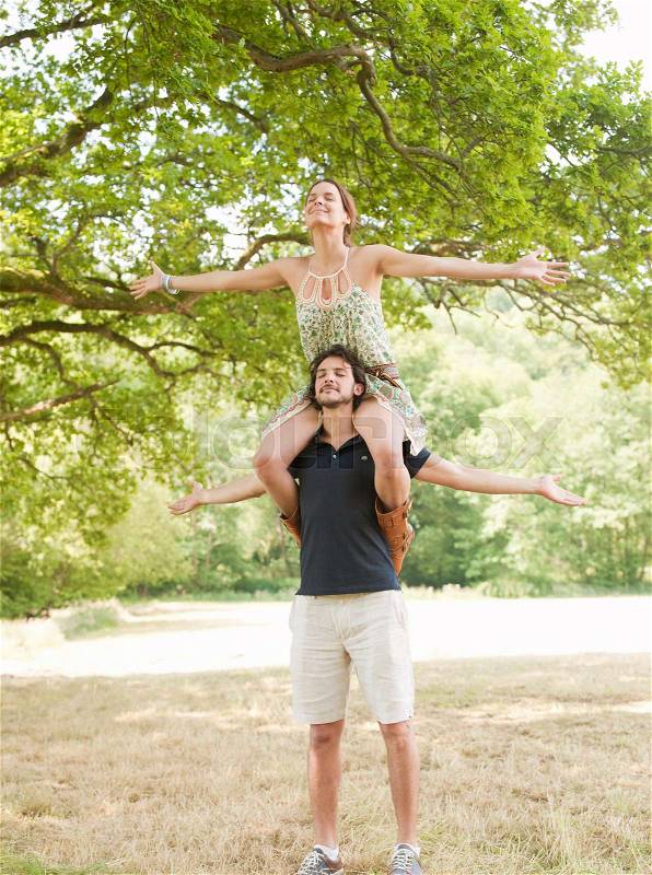 Woman on mans shoulders under tree, stock photo