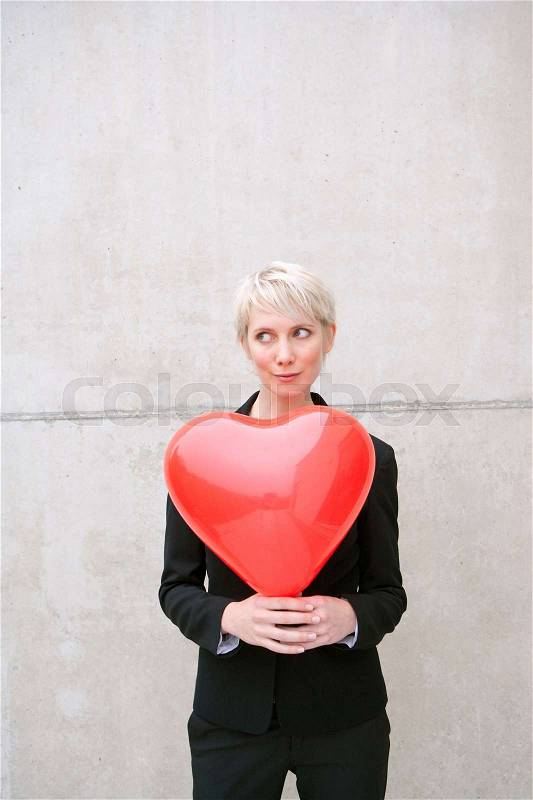 Woman in suit holding heart balloon, stock photo