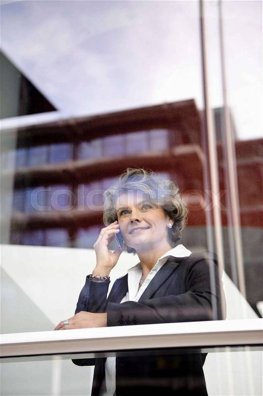 Businesswoman using cell phone, smiling, stock photo