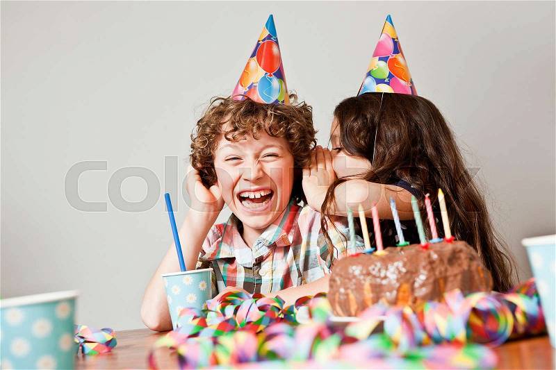Girl whispers in boys ear at birthday, stock photo