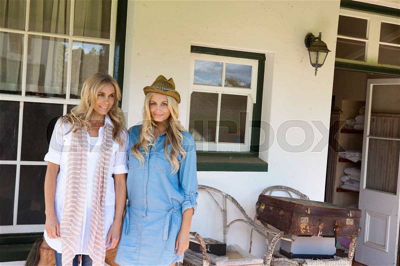 Mother and daughter standing on porch, stock photo