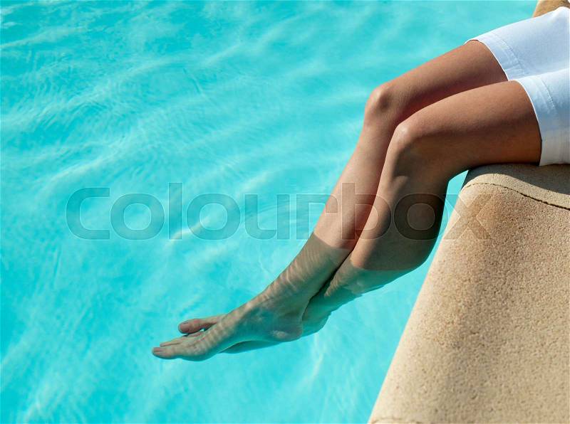 Woman dangling her feet in pool, stock photo