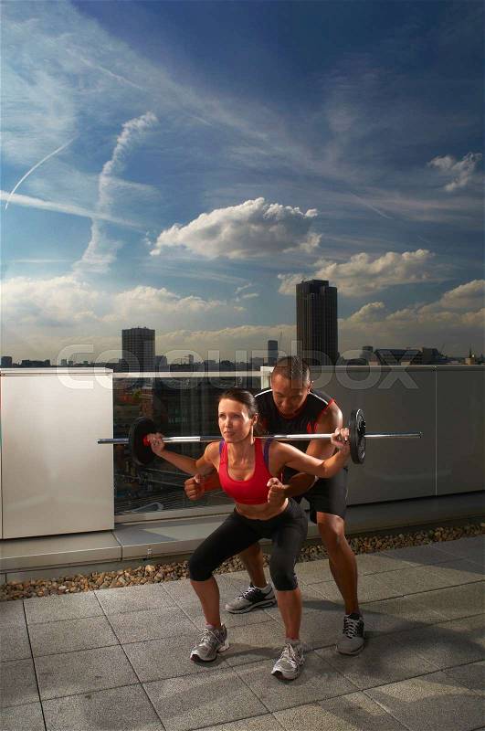 Woman exercising with trainer on rooftop, stock photo