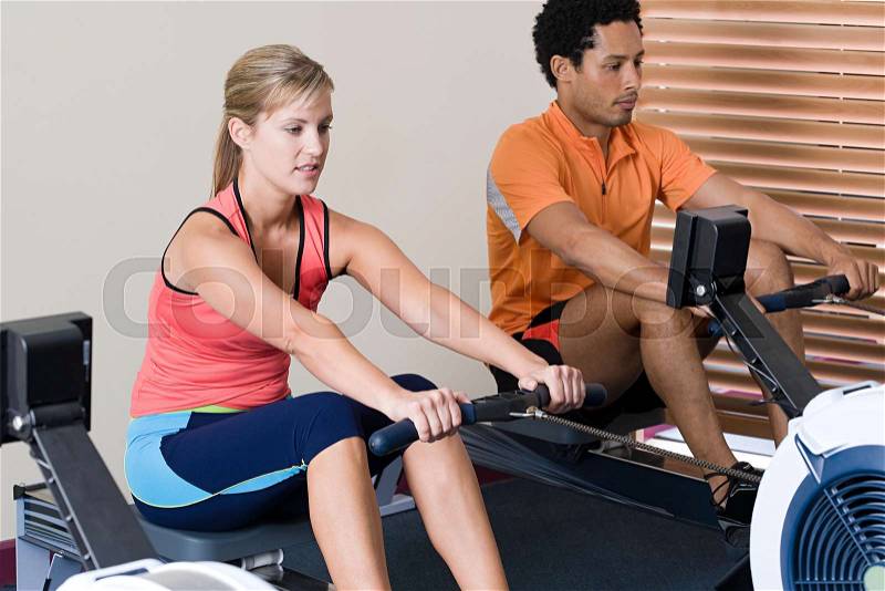 Woman and man on rowing machines, stock photo