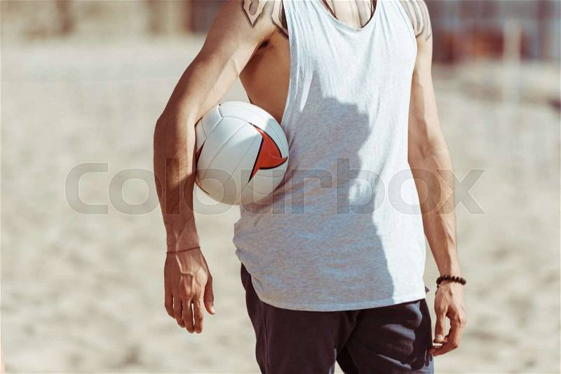 Cropped view of man holding volleyball ball while standing on beach , stock photo