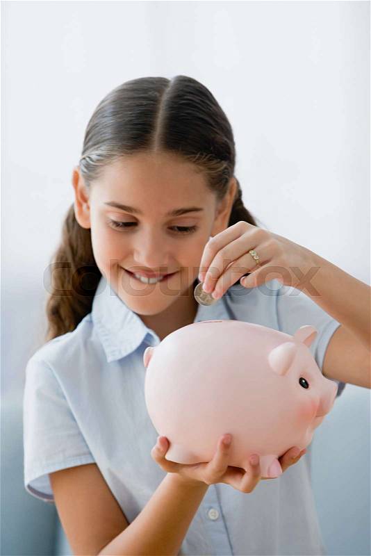 Girl saving a coin in piggy bank, stock photo