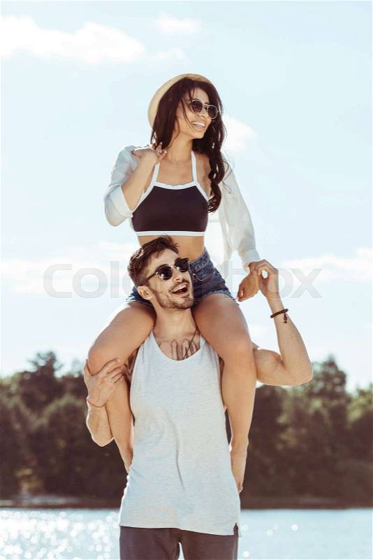 Handsome young man carrying beautiful girl on shoulders at beach, stock photo