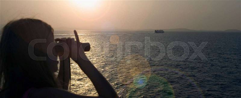 Young girl using binoculars to look at a boat in the water, stock photo