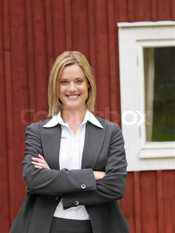 Businesswoman by country cottage smiling, stock photo
