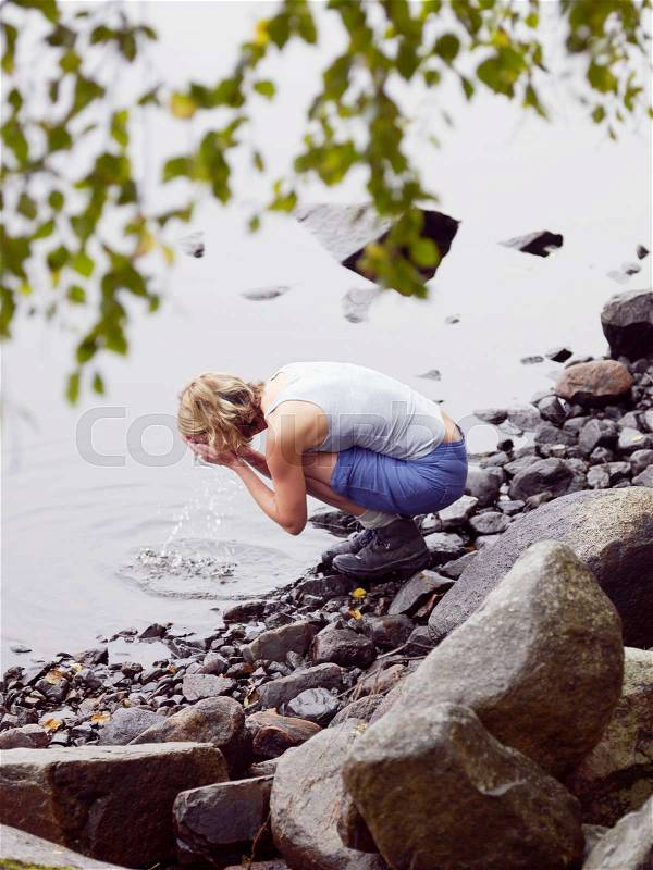 Woman washing face in lake, stock photo