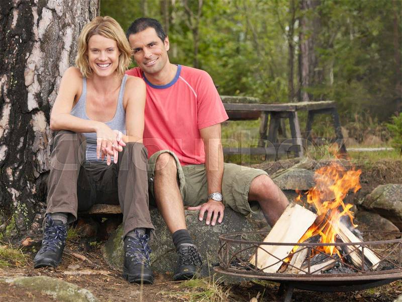 Couple sitting by a fire pit smiling, stock photo