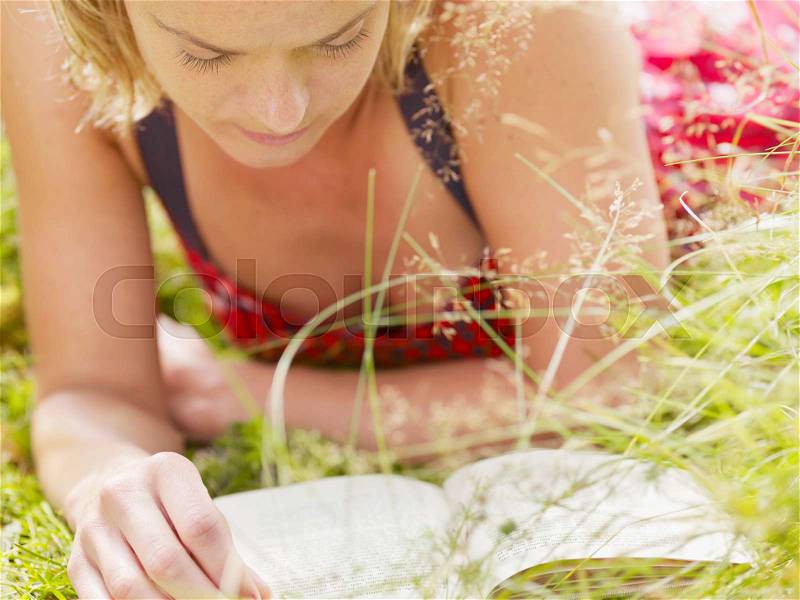 Woman lying in grass reading a book, stock photo