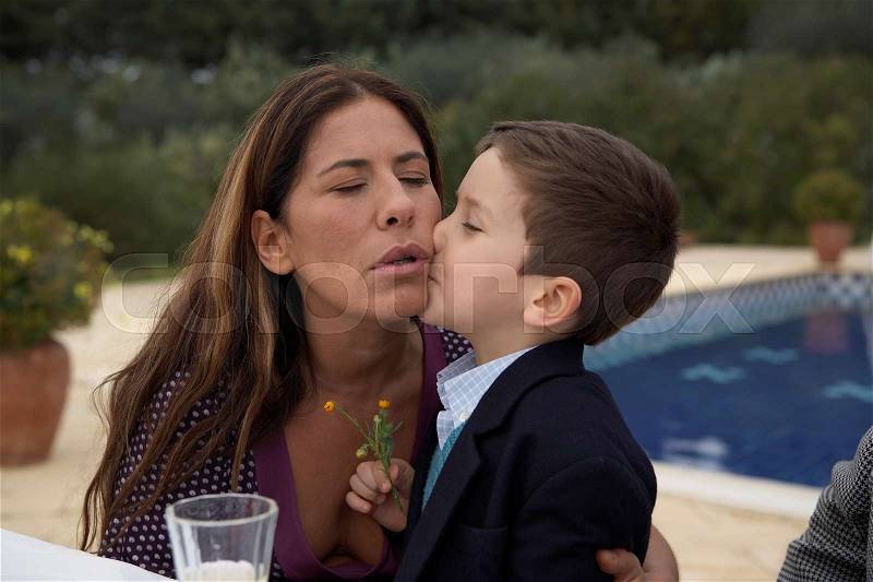 Mother kissing son at the table, stock photo