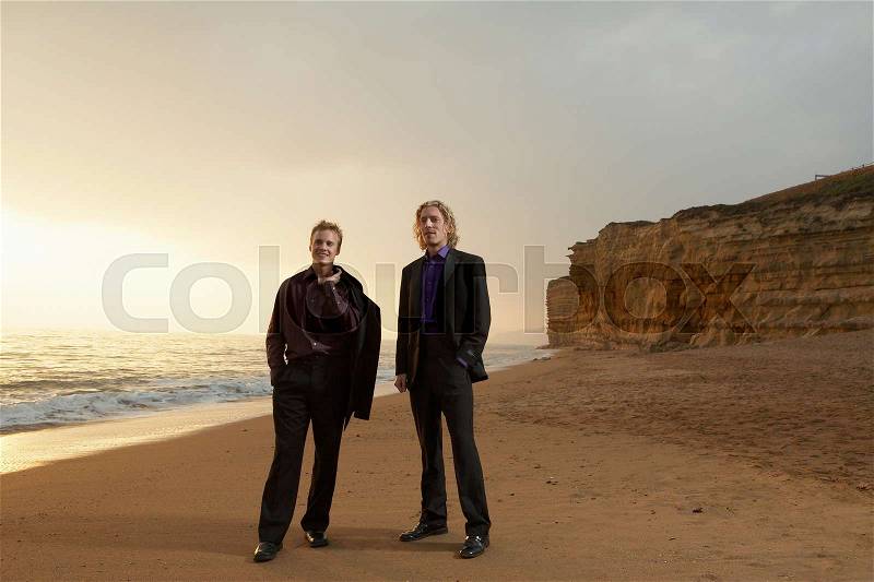 Two men standing on beach at sunset, stock photo